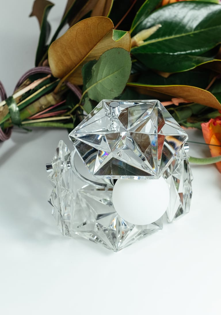 Kinkeldey Mémoire crystal lamp with white globe bulb gleams beside a vivid mixed bouquet on a clean white backdrop.