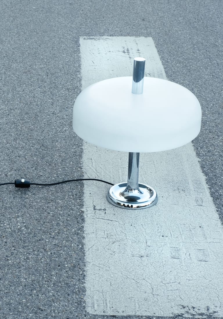 Frosted-dome chrome mushroom lamp staged on worn zebra-crossing stripe, black cord trailing over grey asphalt.