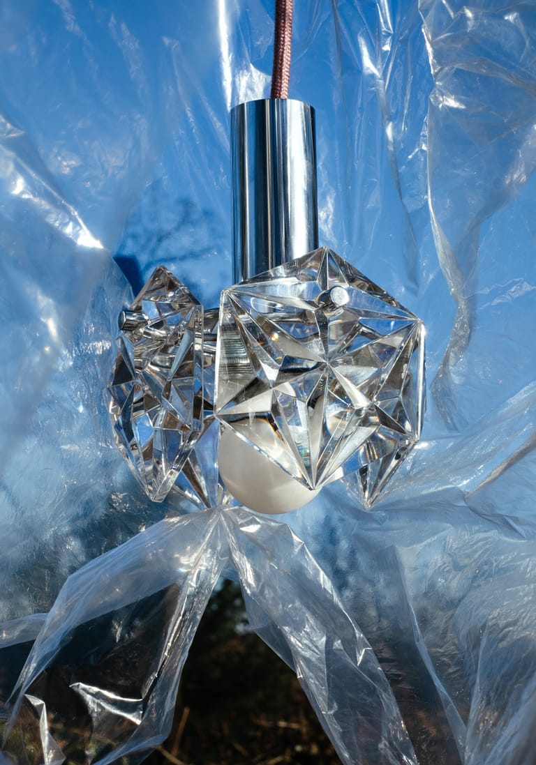 Crystal Kinkeldey Memoire pendant with chrome stem glints through crinkled clear film against vivid blue sky.