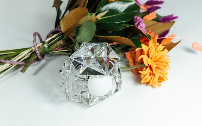 Kinkeldey Mémoire crystal lamp with white globe bulb gleams beside a vivid mixed bouquet on a clean white backdrop.